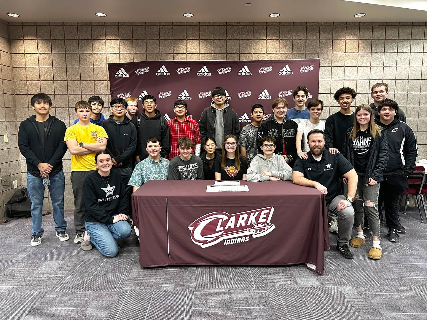 Claire Jacobsen signs her letter of intent Jan. 30 to run cross country at Indian Hills Community College. She is pictured in the center with the Clarke Cross Country team and coaches.