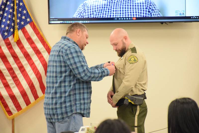 Russ Jacobson pins a lifesavers award on Clarke County Sheriff’s Deputy Wayne Keeler’s shirt. Keeler helped save Jacobson’s life after a motorcycle accident in October by applying a lifesaving tourniquet.