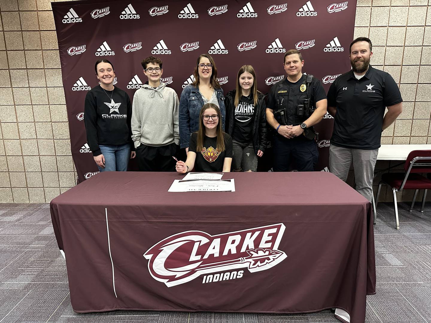 Claire Jacobsen signs her letter of intent Jan. 30 to run cross country at Indian Hills Community College. She is pictured with from left, Clarke cross country coach Abby Loecke, brother Cole, mom Carissa, sister Chloe, dad Curt and Clarke cross county head coach Thomas Kedley.